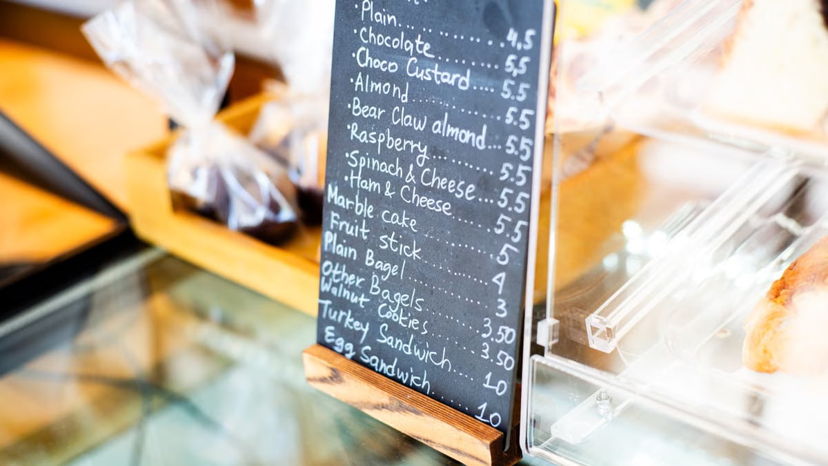 Chalkboard menu listing bakery items like croissants and sandwiches in a cafe setting.